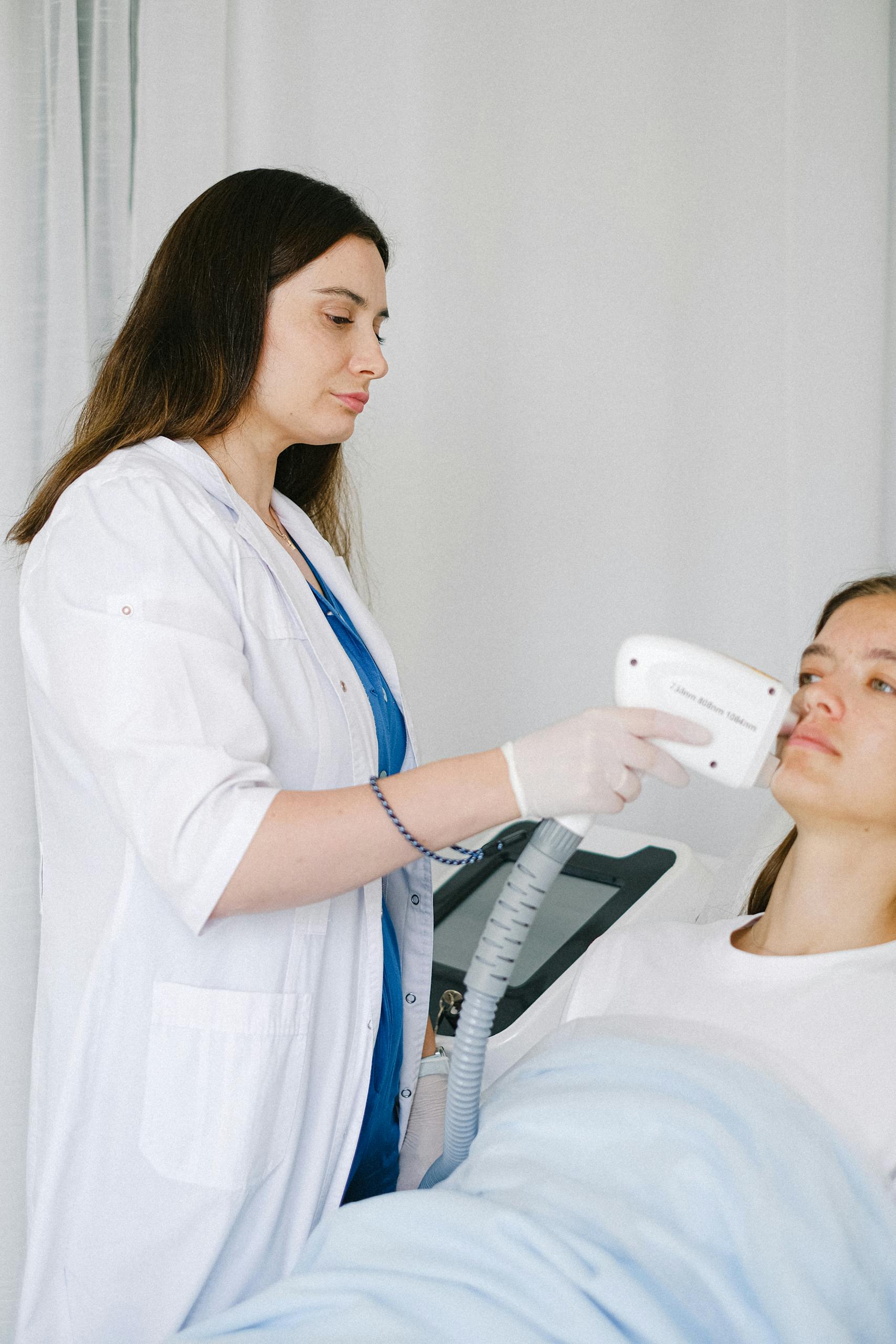 Female specialist performing laser therapy on patient at clinic